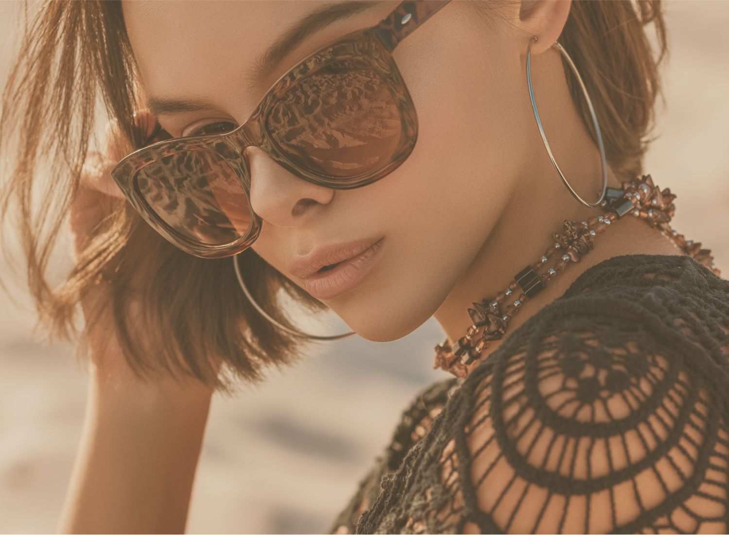 Woman wearing sunglasses and jewelry outdoors.